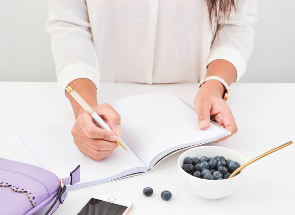 woman taking notes with a bowl of blueberries next to her low carb foods