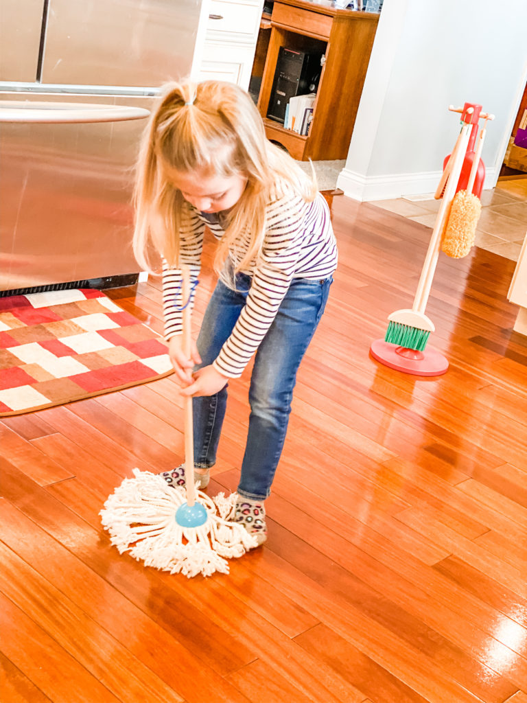 little girl mopping hardwood floor as a part of her chores