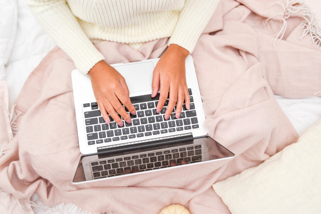 woman typing on laptop with a pink blanket on her lap. Searching topic advice on kids and chores. 